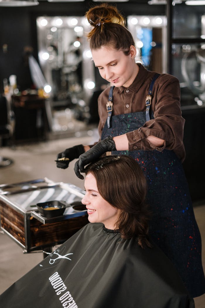 Hairdresser applying color to woman's hair in a modern salon, capturing a lively professional atmosphere.